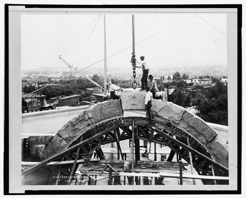 Construction workers on a wooden scaffold set the keystone into a stone arch